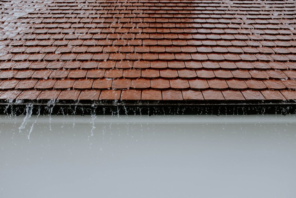 Fuite de toit dans le Valenciennois : intervention d'urgence sous 24h par votre couvreur artisan 2 Brown roof tiles with rainwater cascading down, showcasing architectural texture and detail.