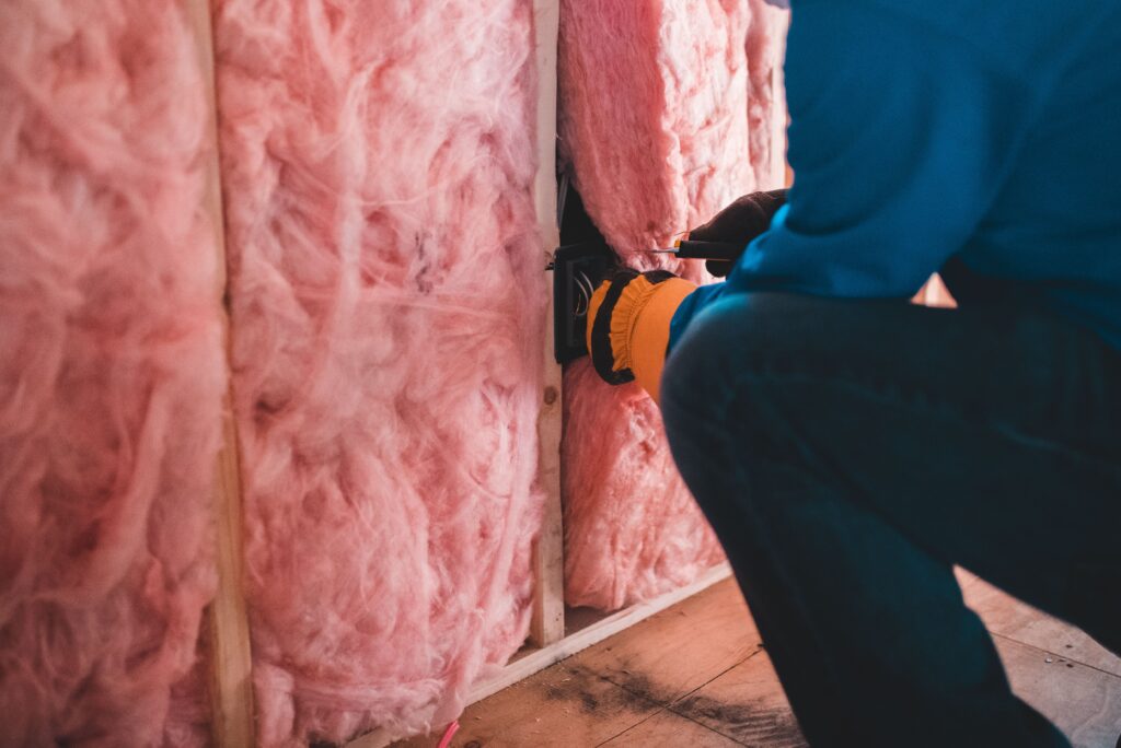 Crop unrecognizable worker in gloves sitting on haunches and insulating with pink stone wool