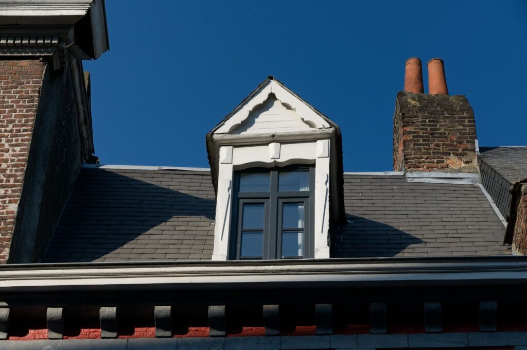 A stunning architectural detail of a rooftop with a window and brick chimney under a clear blue sky.